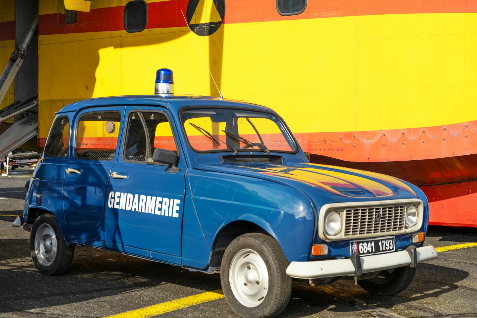 Classic blue gendarmerie car in front of yellow backdrop, evoking a nostalgic feel.